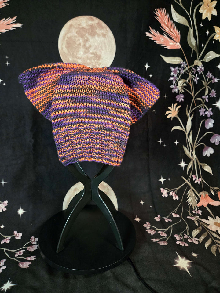Colorful knitted Cat Hat on display, featuring vibrant purple and orange patterns, perfect for all ages.