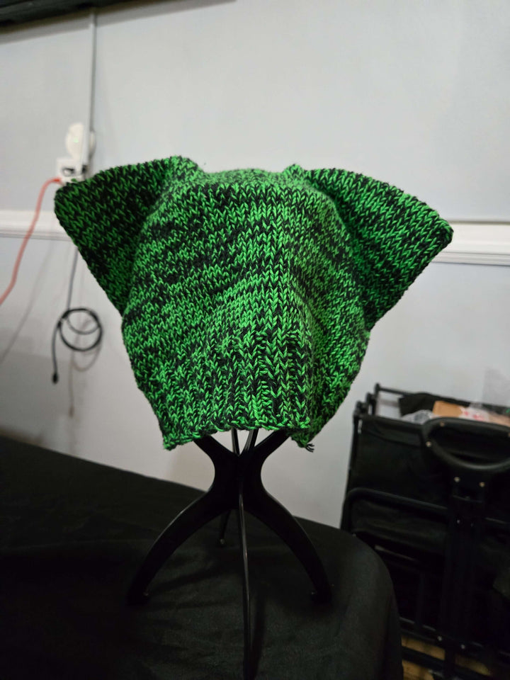 Green knitted Cat Hats with ears displayed on a stand, perfect for kids and adults.