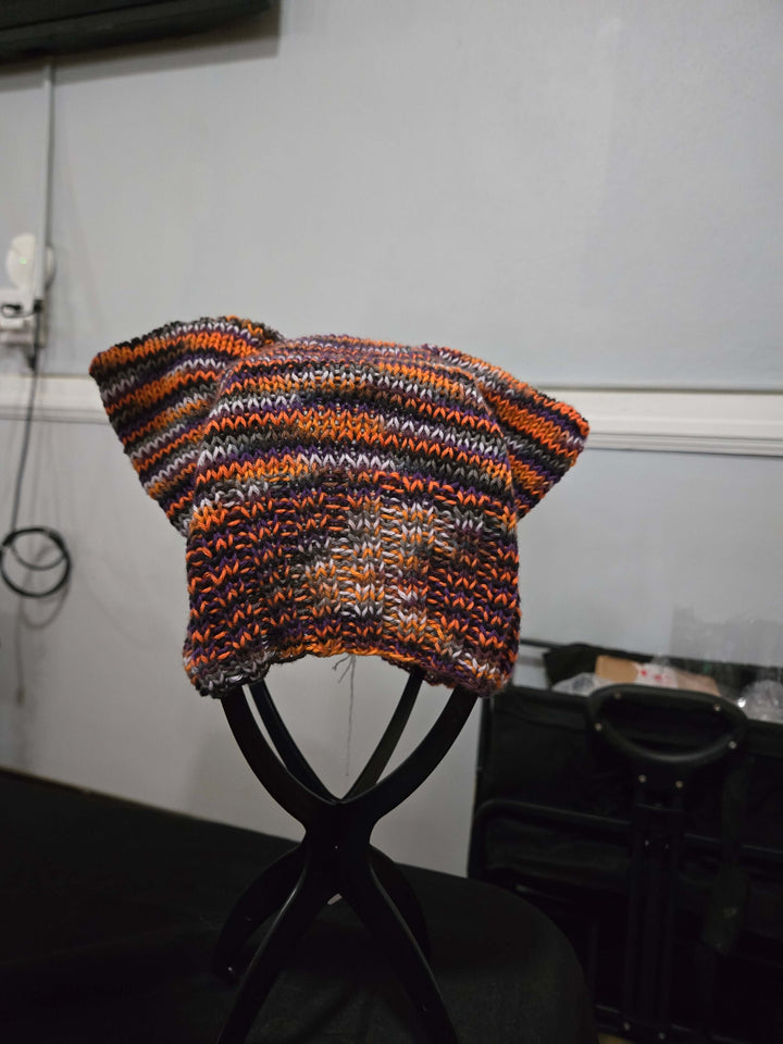 Handmade Cat Hats with colorful knitted pattern and ear flaps displayed on a black stand.